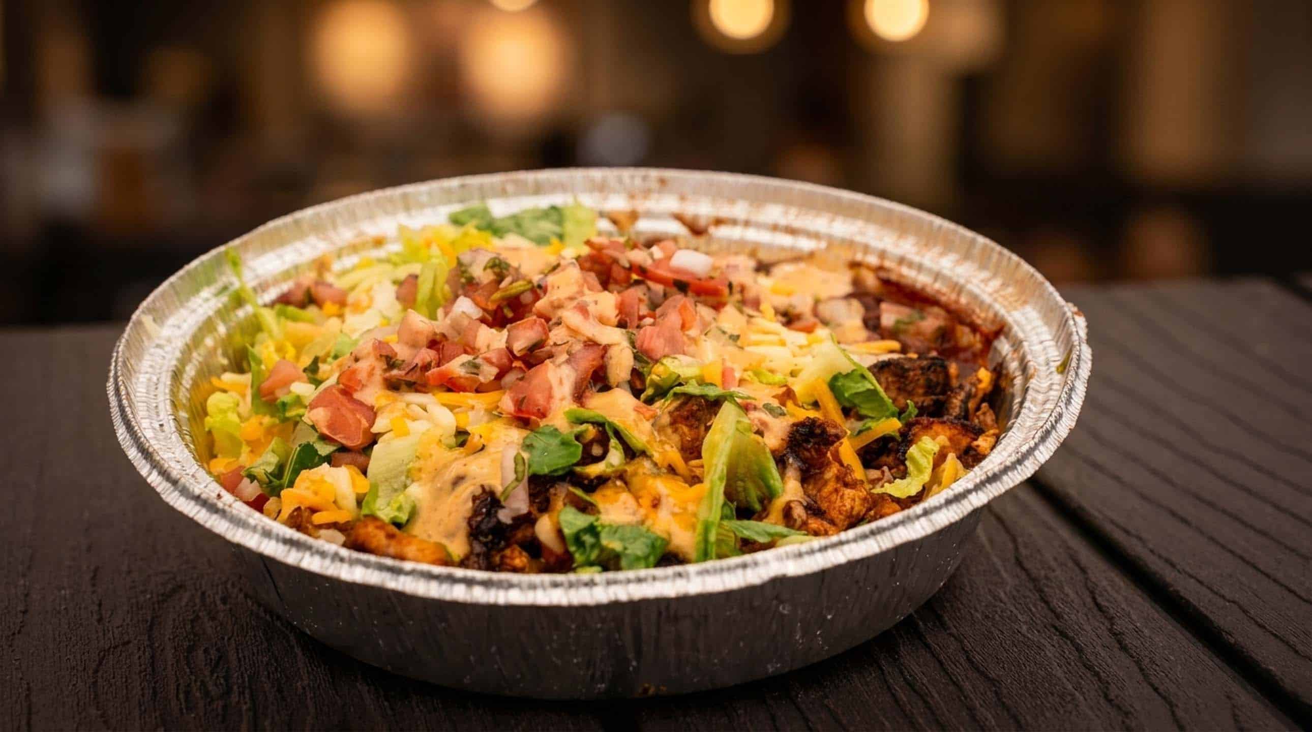 A loaded burrito bowl topped with shredded cheese, lettuce, pico de gallo, and chipotle mayo